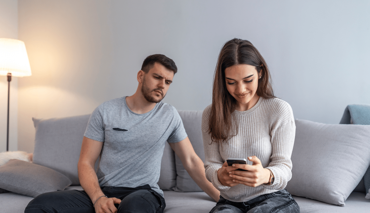 Homme et femme assis sur un canapé, elle regarde son téléphone