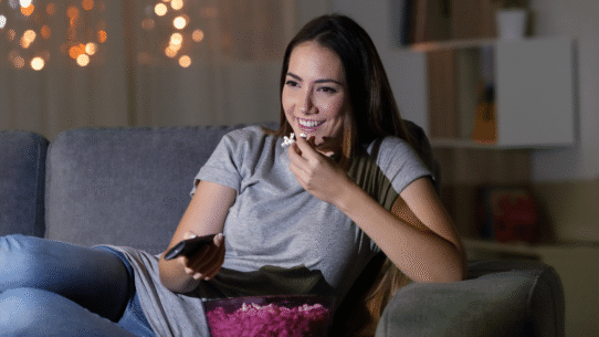 Femme souriante mangeant du pop-corn devant la télévision