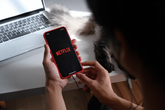 Personne utilisant Netflix sur un smartphone près d'un ordinateur portable