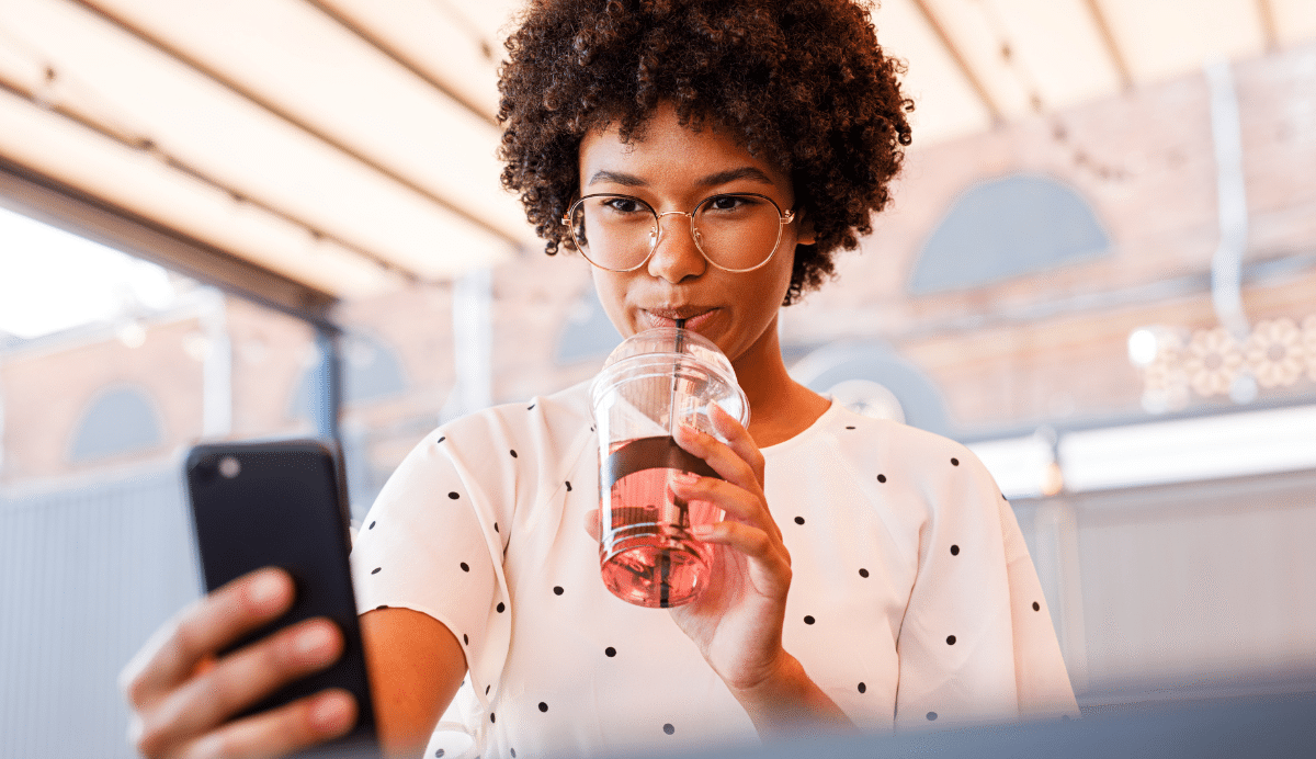 Femme avec lunettes buvant une boisson et utilisant un smartphone