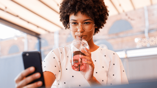 Femme avec lunettes buvant une boisson et utilisant un smartphone