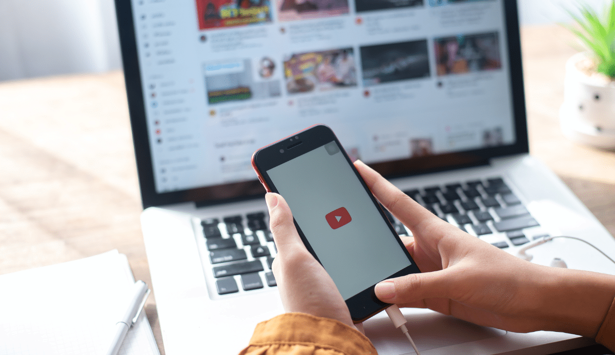 Personne utilisant un smartphone devant un ordinateur avec YouTube
