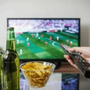 Main tenant une télécommande devant un match de football à la télévision