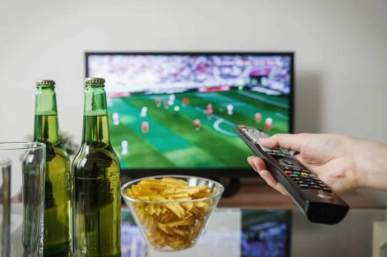 Main tenant une télécommande devant un match de football à la télévision