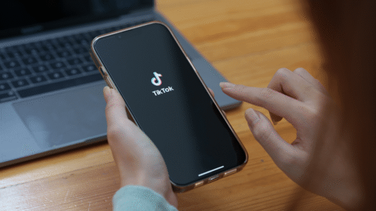 Personne utilisant TikTok sur un smartphone devant un ordinateur