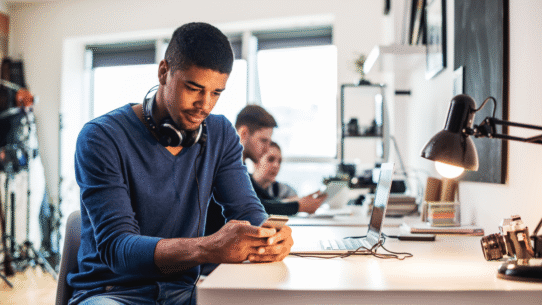 Homme avec casque autour du cou utilisant un smartphone au bureau