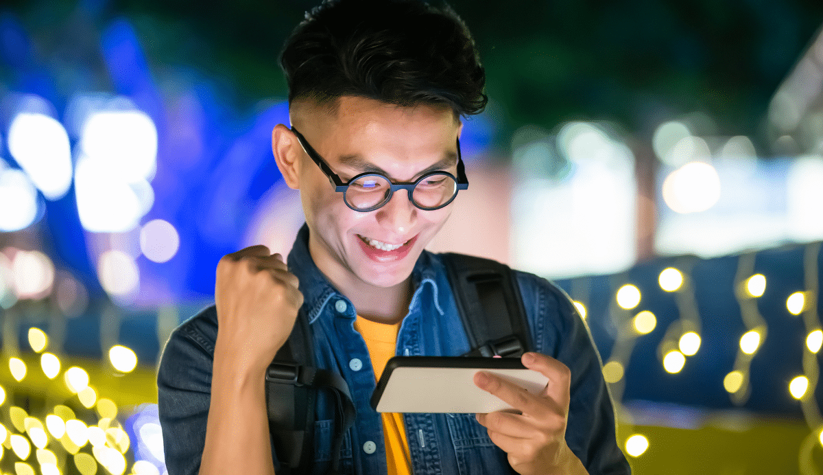 Homme souriant levant le poing en regardant son smartphone