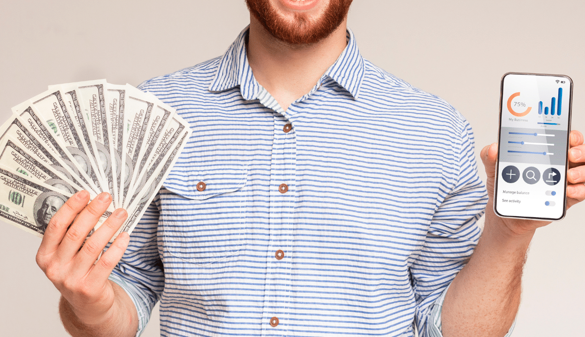 Homme souriant avec des billets de banque et un smartphone affichant des graphiques