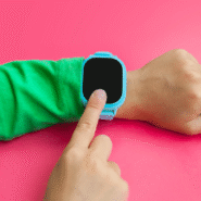 Montre connectée bleue sur le poignet d'un enfant sur fond rose