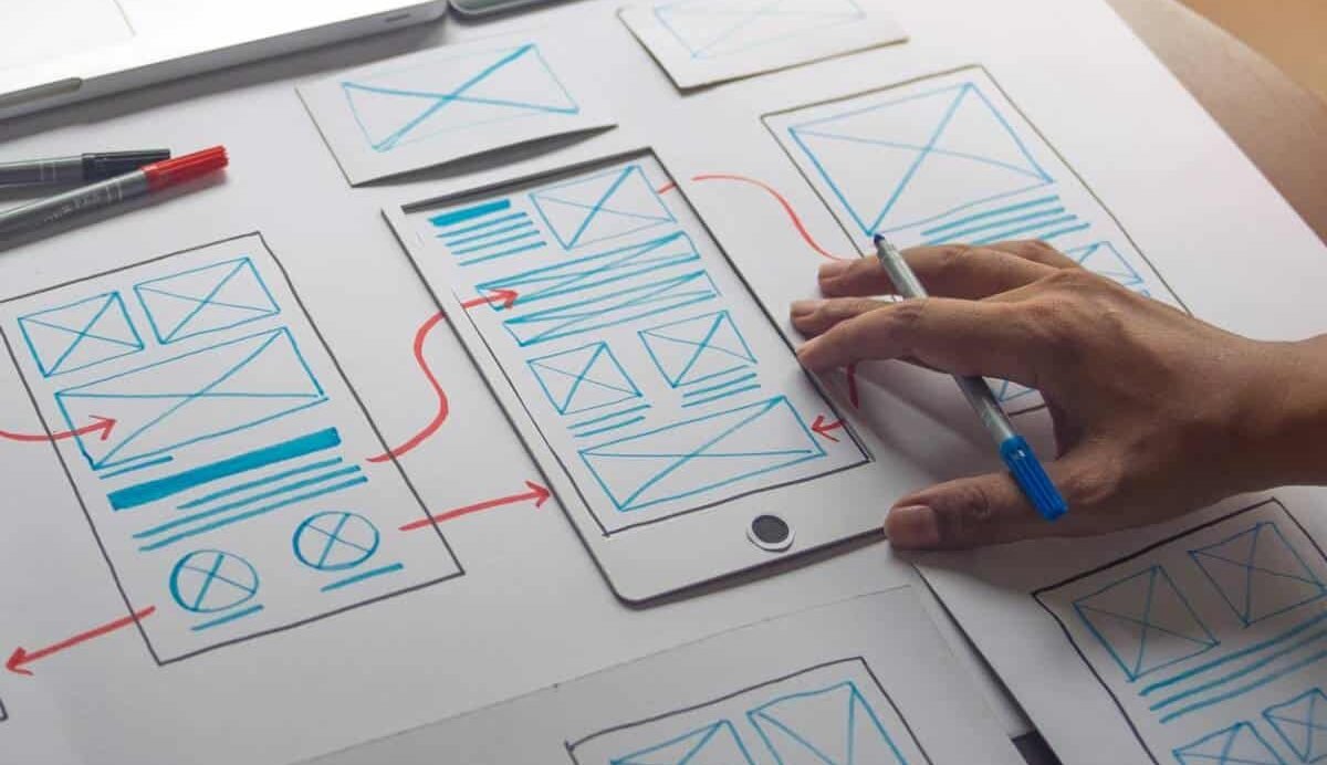 Maquettes de conception d'interface mobile sur papier avec une main dessinant
