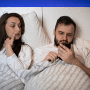 Un couple au lit, l'homme regarde un smartphone