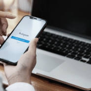 Personne utilisant Instagram sur un smartphone devant un ordinateur portable