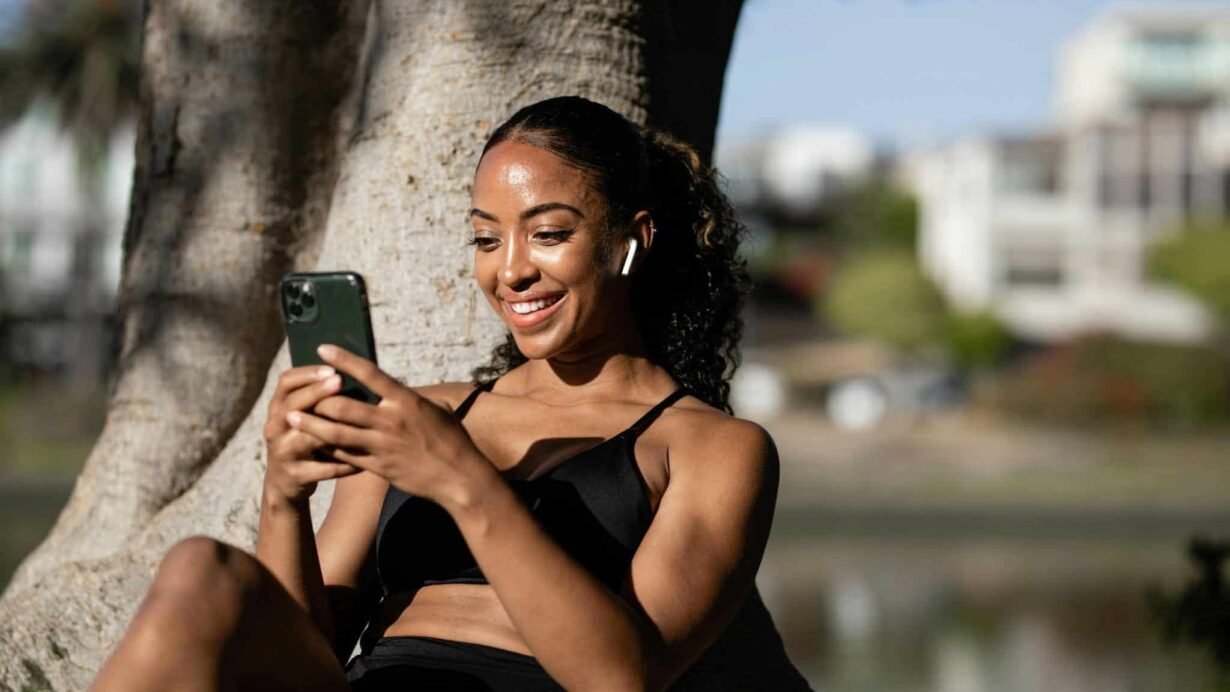 Femme souriante utilisant un smartphone sous un arbre