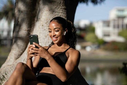 Femme souriante utilisant un smartphone sous un arbre