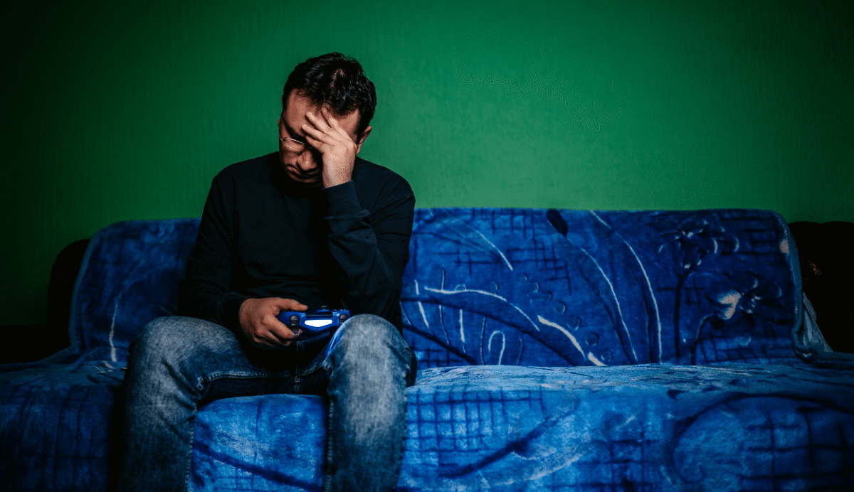 Homme assis sur un canapé bleu tenant une manette
