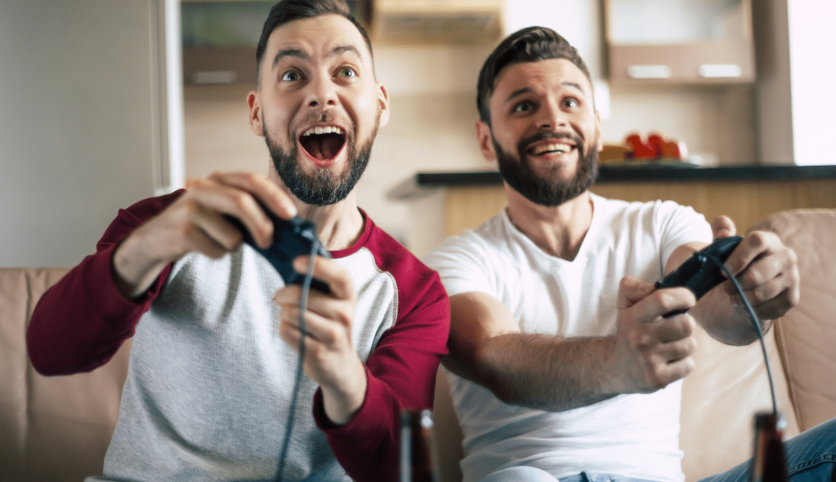 Deux hommes souriants jouent à un jeu vidéo sur un canapé
