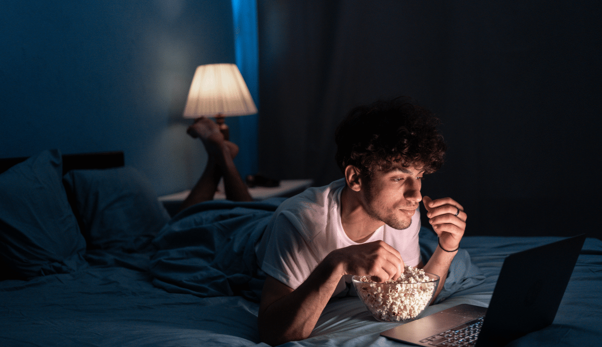 Homme mangeant du pop-corn en regardant un film sur un ordinateur portable