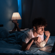 Homme mangeant du pop-corn en regardant un film sur un ordinateur portable