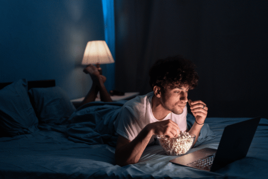 Homme mangeant du pop-corn en regardant un film sur un ordinateur portable