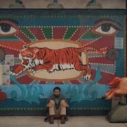 Homme assis devant une fresque murale avec un tigre et des affiches