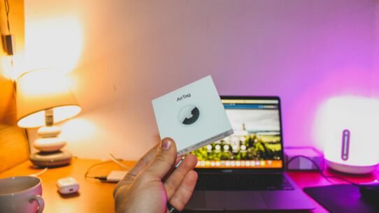 Une main tenant une boîte d'AirTag devant un bureau avec un ordinateur portable