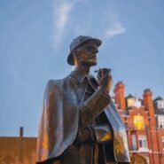 Statue en bronze d'un détective avec une pipe devant des bâtiments