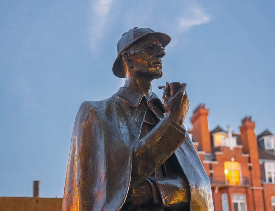 Statue en bronze d'un détective avec une pipe devant des bâtiments