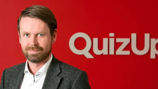 Homme en costume devant un fond rouge avec le logo QuizUp