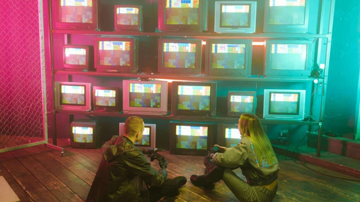 Deux personnes assises devant des télévisions rétro affichant des motifs colorés