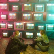 Deux personnes assises devant des télévisions rétro affichant des motifs colorés
