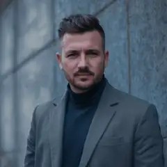 Homme en costume gris devant un mur en pierre