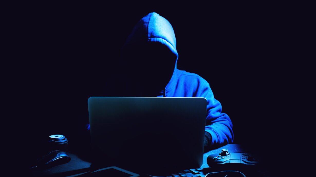 Un homme capuché derrière un ordinateur